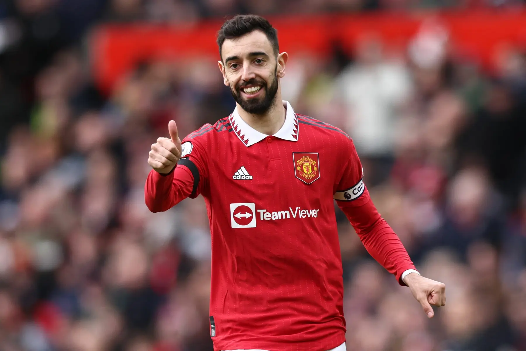 Bruno Fernandes smiling and giving a thumbs up while wearing a red Manchester United home kit