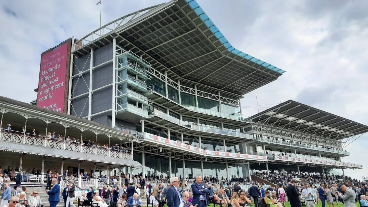 The large modern grandstand at York Racecourse with crowds of people and a red welcome banner.