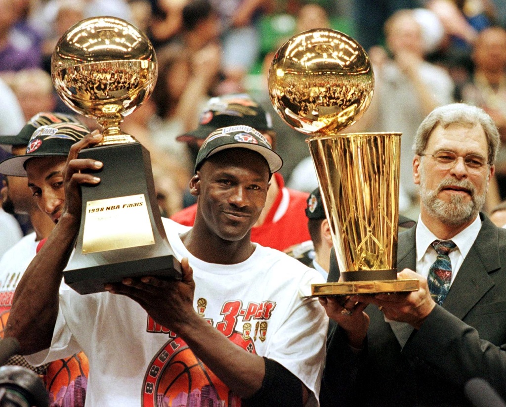 Michael Jordan, the center of one of the most hotly-debated NBA myths, holds up a championship trophy