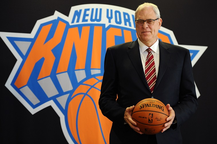 Phil Jackson holding a basketball and posing in front of the New York Knicks logo