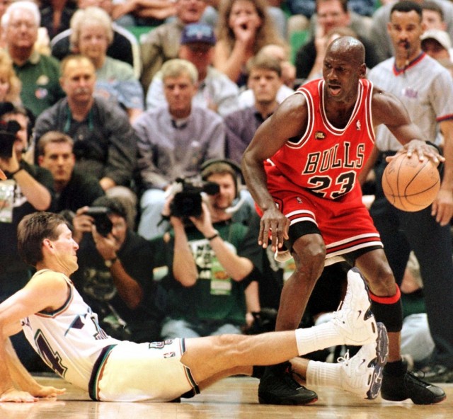  Michael Jordan intenta pasar la pelota por encima de un oponente que ha caído al suelo.