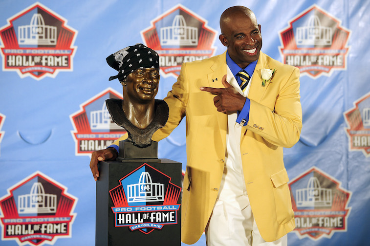 Deion Sanders smiles next to his Hall of Fame bust.