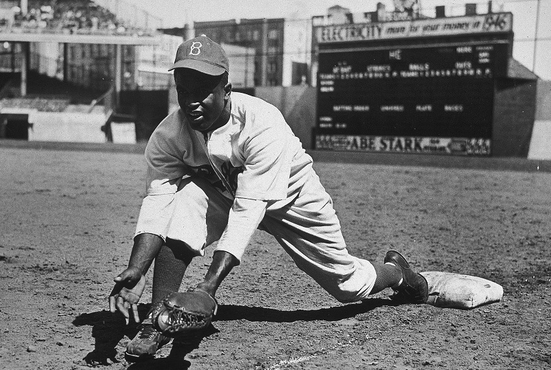 American baseball player Jackie Robinson (1919 - 1972) grounds a ball at first place while warming up for an exhibition game against the New York Yankees, Ebbets Field, NYC, 1950s.