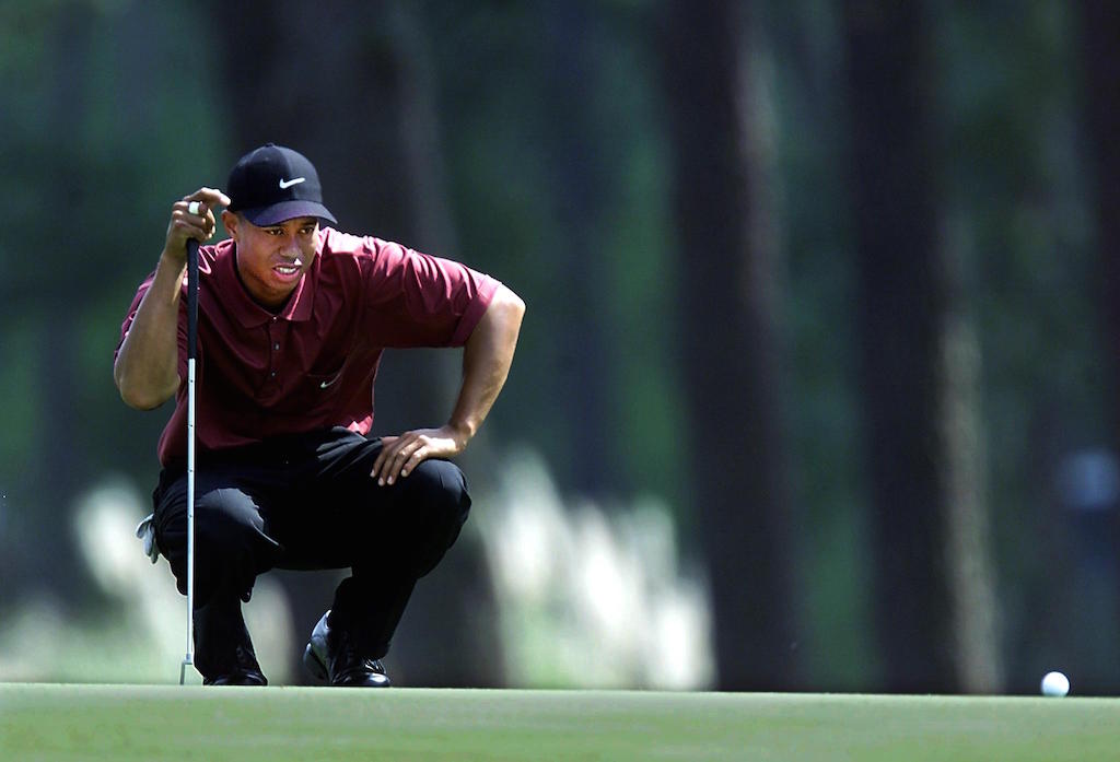 Tiger Woods kneels on the green to assess his situation.