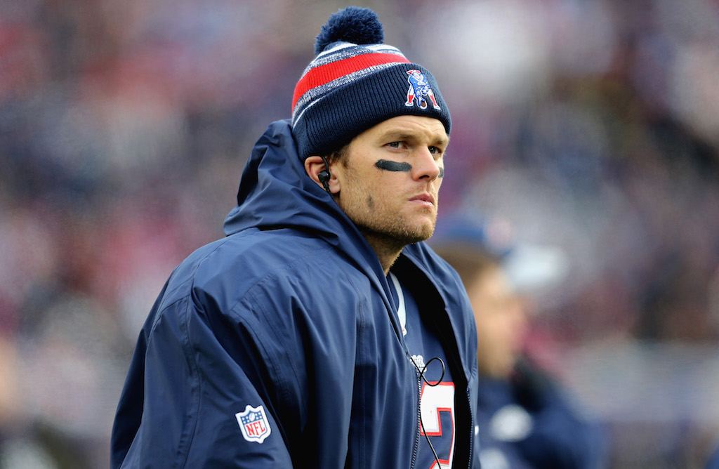Tom Brady sits on the sidelines and pensively looks at the field.