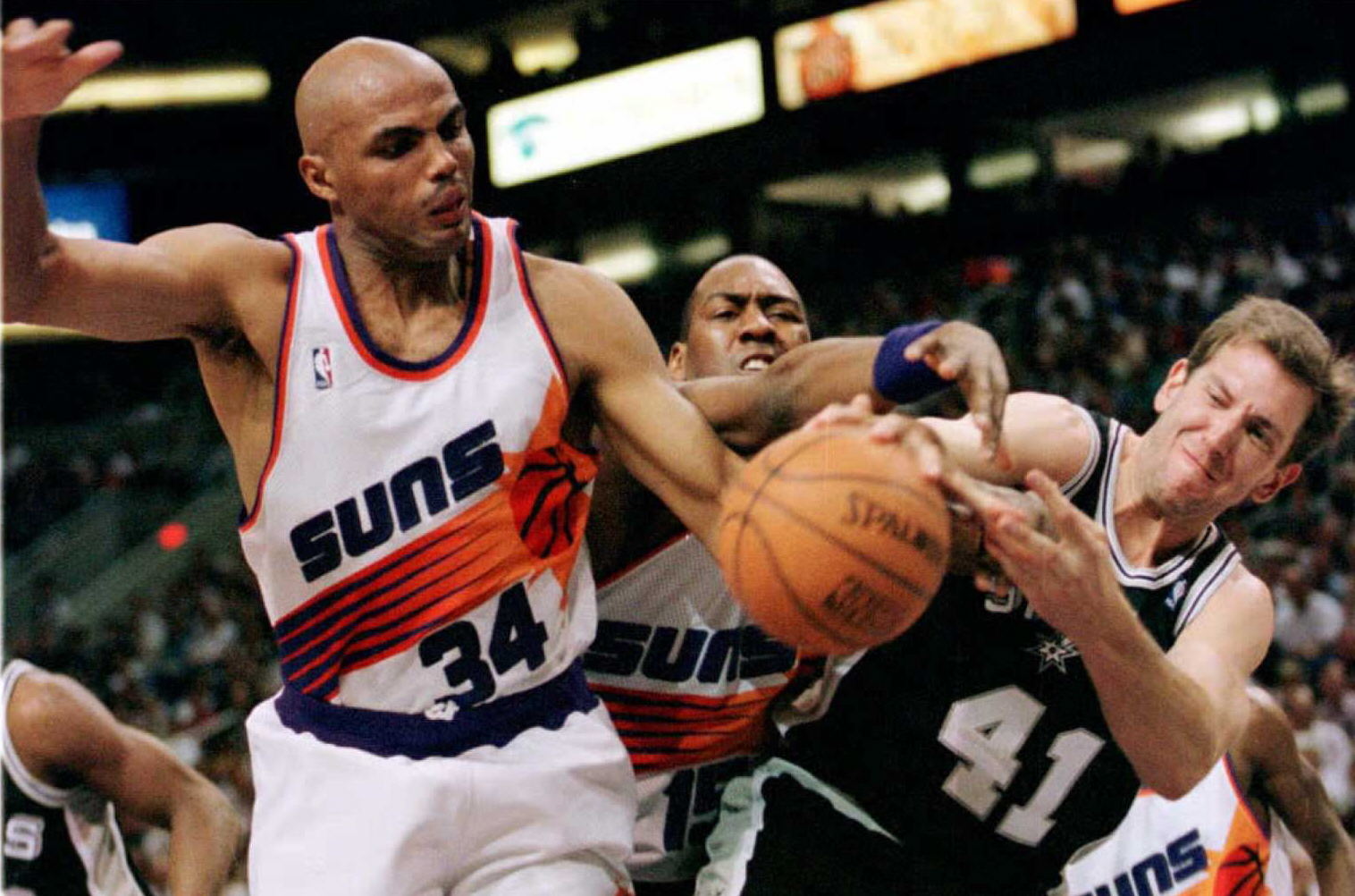 Charles Barkley tries to control the ball against an opposing team member.