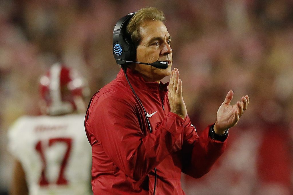 Nick Saban clapping his hands while wearing a black headset on the field. 