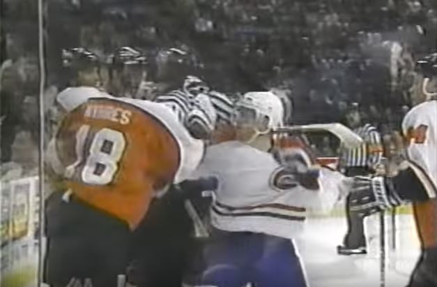 Members of opposing hockey teams fighting up against the glass during a game.