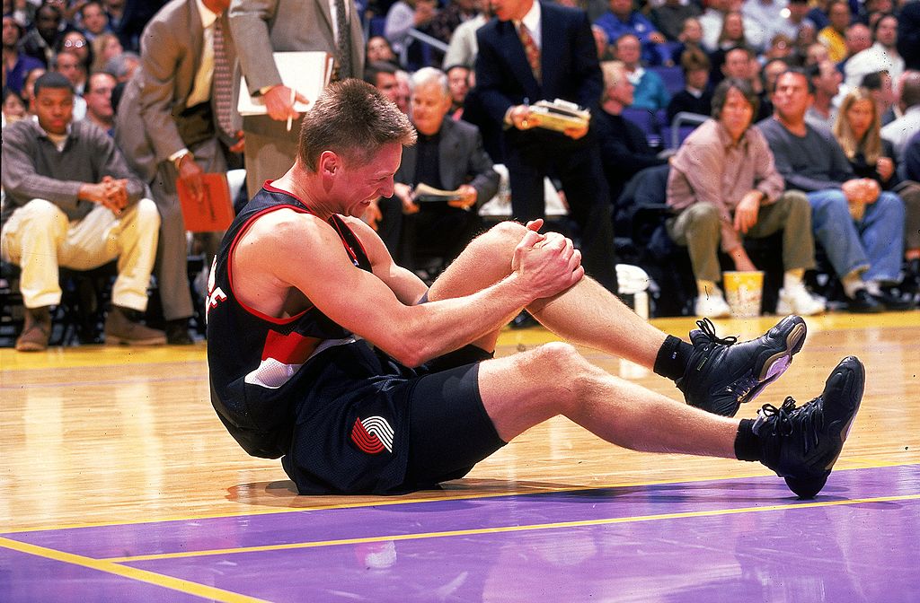 Detlef Schrempf de Portland TrailBlazers se sienta en la cancha sosteniendo su rodilla