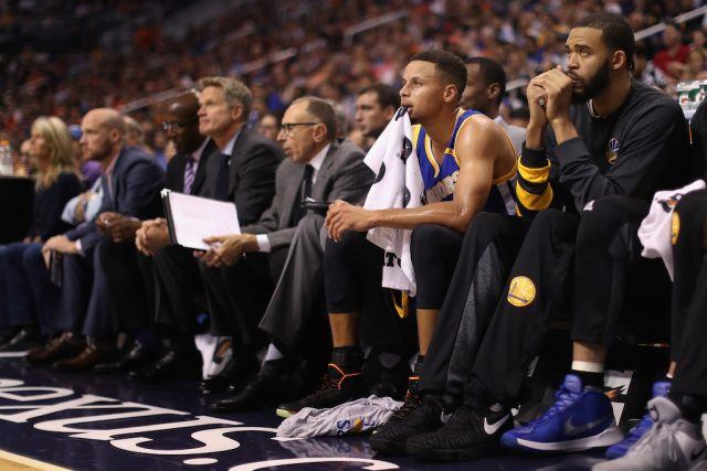 Stephen Curry sits on the bench and watches play.