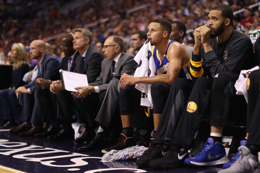 Stephen Curry sits on the bench and watches play.