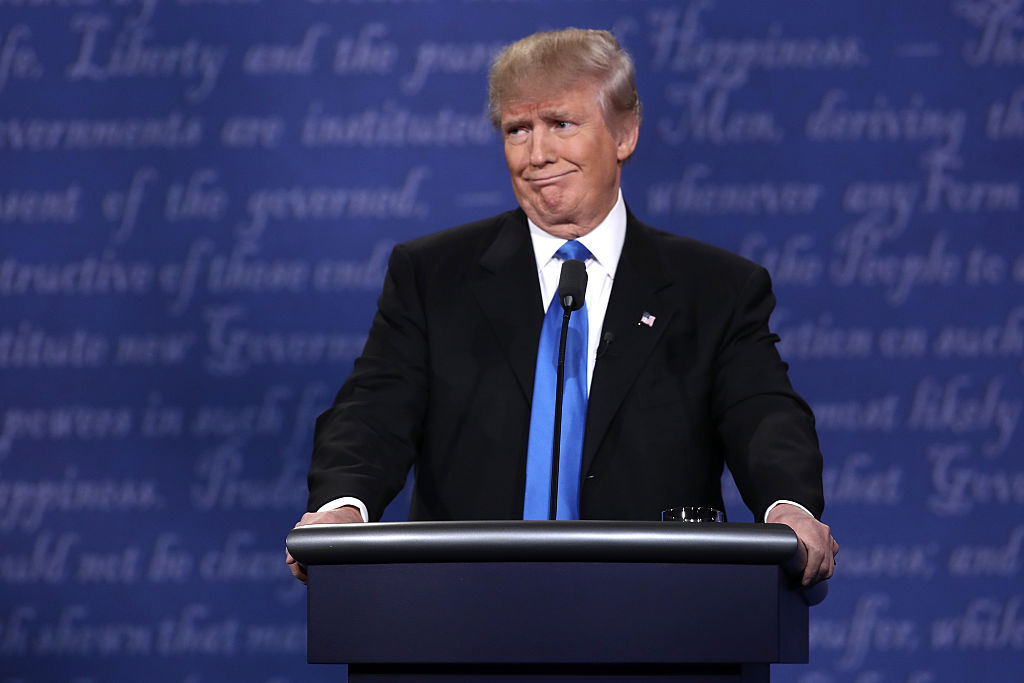 Donald Trump stands behind a large black podium. 
