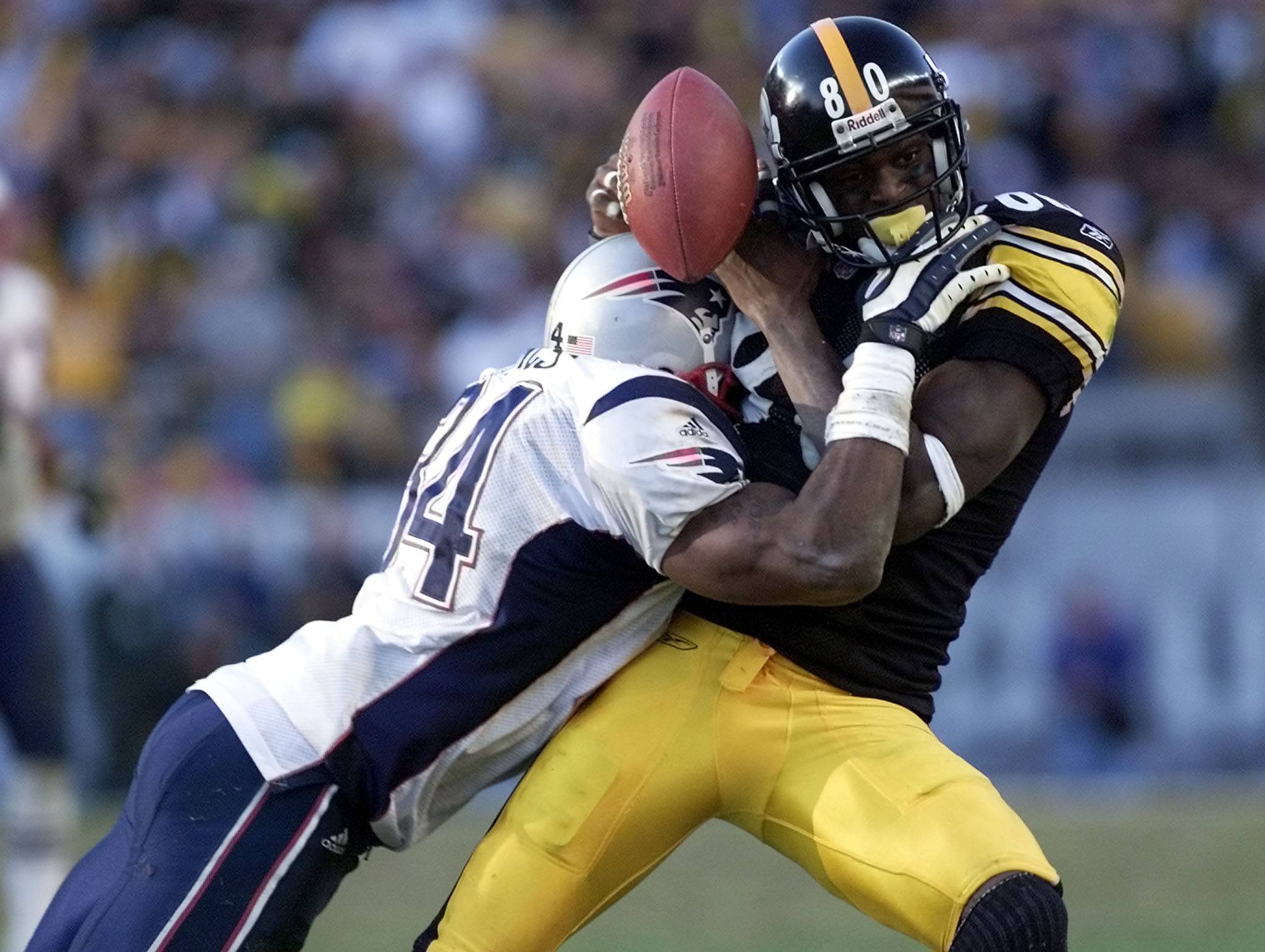 New England Patriots Tebucky Jones (L) hits Pittsburgh Steelers wide receiver Plaxico Burress (R) knocking the ball out of his hands for an incomplete pass in the fourth quarter of the AFC Championship game 27 January, 2002 at Heinz Stadium in Pittsburgh, PA. The winner will face either the St. Louis Rams or the Philadelphia Eagles in the Super Bowl. two football players hitting each other