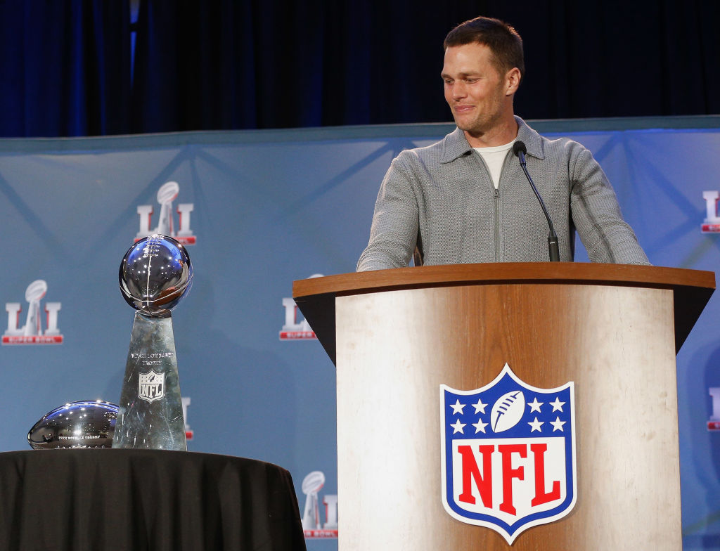 Tom Brady stands at a podium with the Super Bowl Trophy next to him