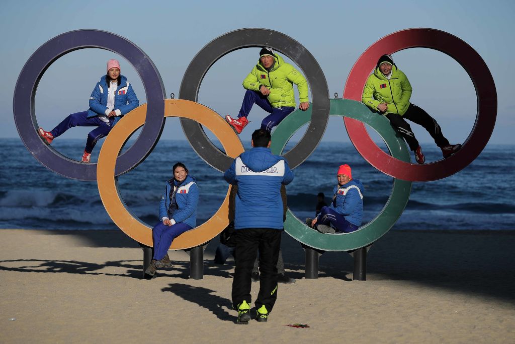 Members of the Mongolian ski team take selfies with the Olympic Rings on the beach at Gangneung.