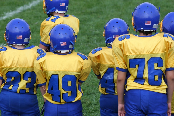 Kids in football uniforms on the sidelines.