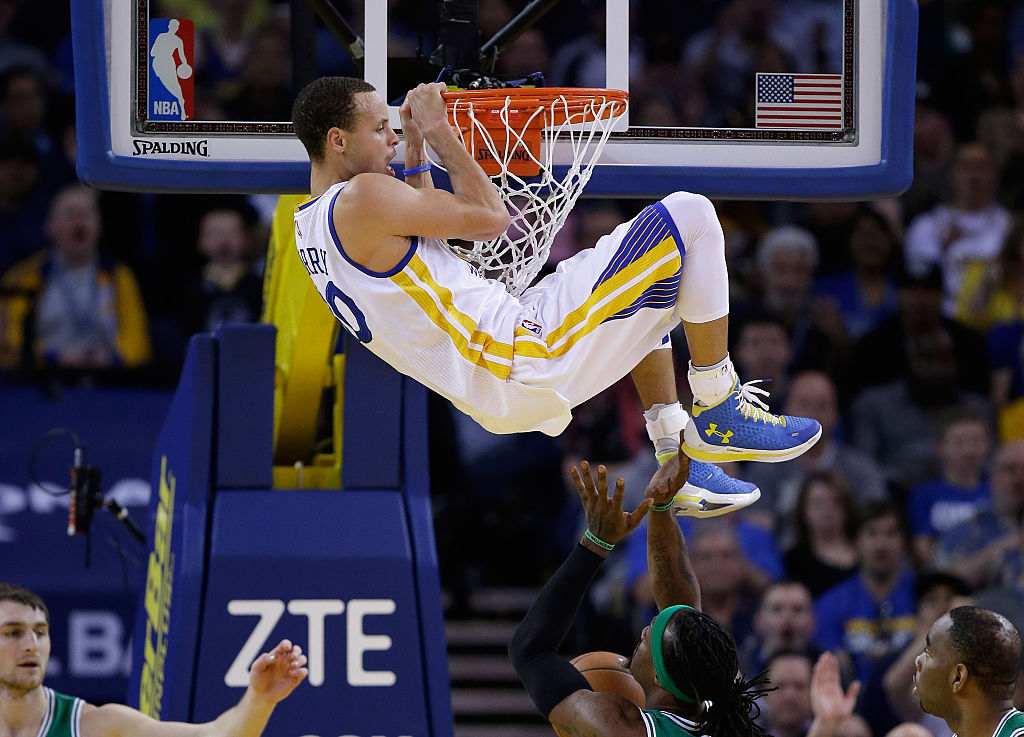Golden State Warriors player Steph Curry hanging onto the rim after dunking