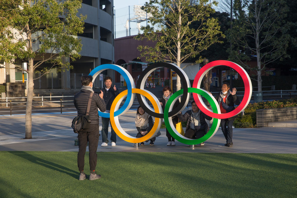 A man takes a photo of people posing behind the Olympic Rings near the New National Stadium in Tokyo.