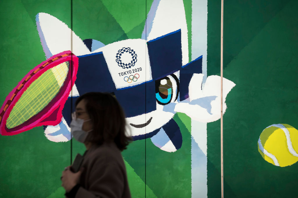 A pedestrian wearing a face mask walks past a display with an illustration of the 2020 Tokyo Olympic and Paralympic Games mascot Miraitowa