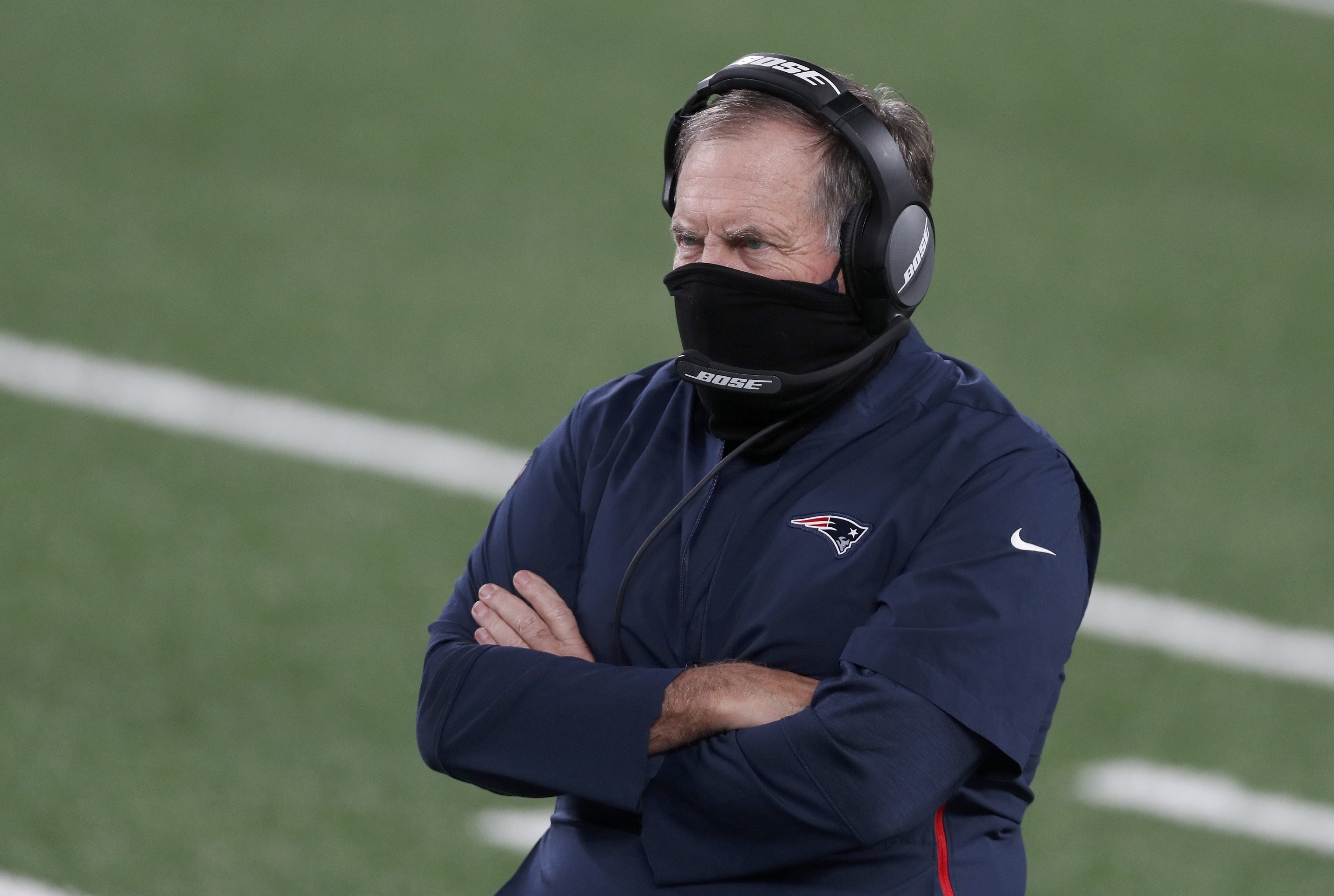 Bill Belichick coaching from the sideline wearing a mask