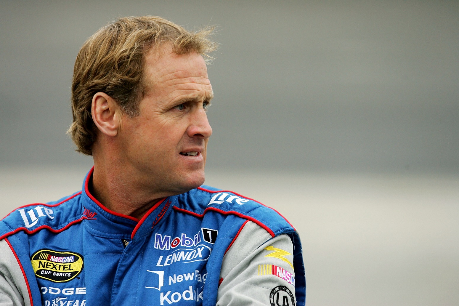 NASCAR driver Rusty Wallace stands on the track and looks off into the distance while wearing his suit