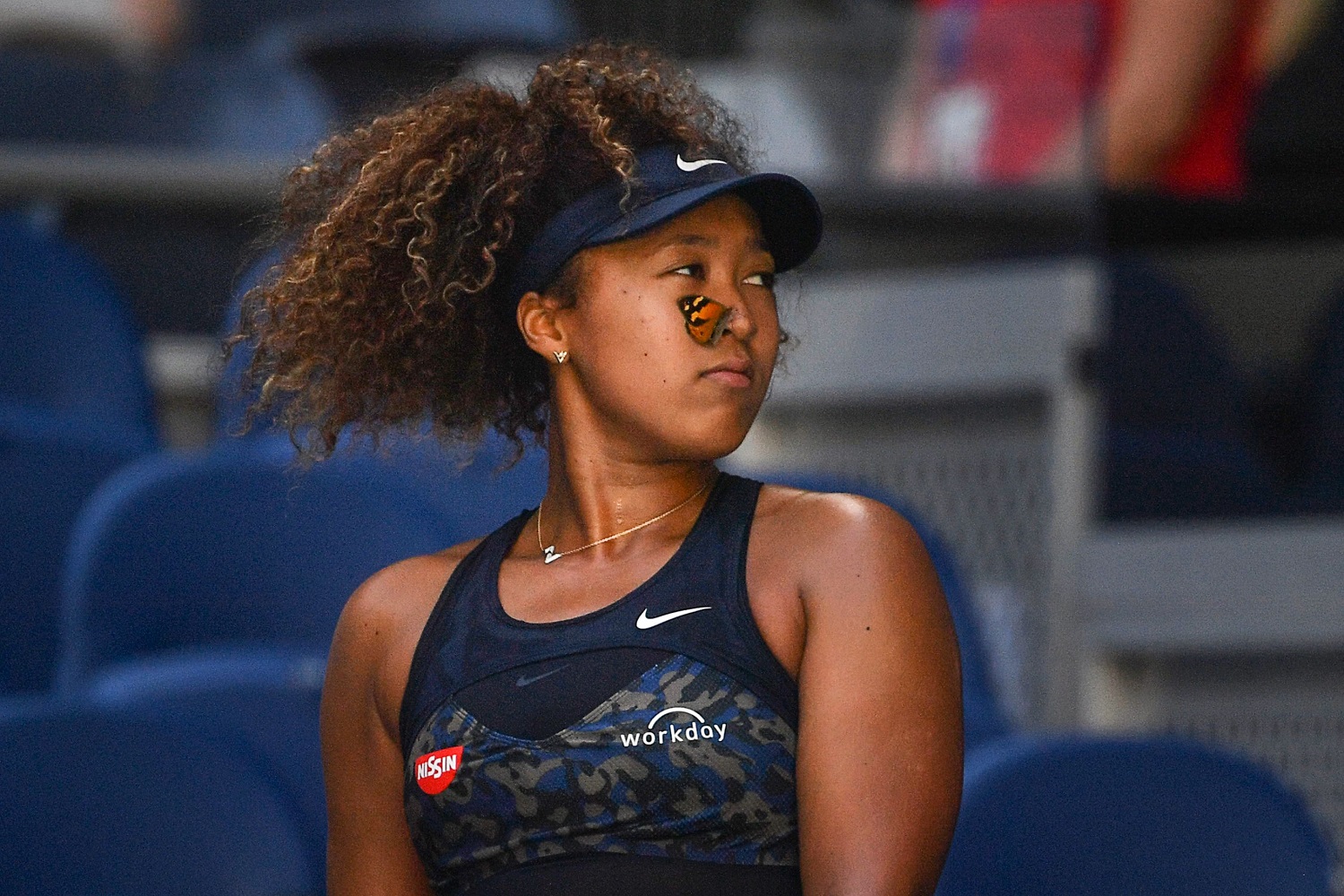 A butterfly lands on Japan's Naomi Osaka as she plays against Tunisia's Ons Jabeur during their women's singles match at the Australian Open tennis tournament in Melbourne. | Paul Crock/AFP via Getty Images
