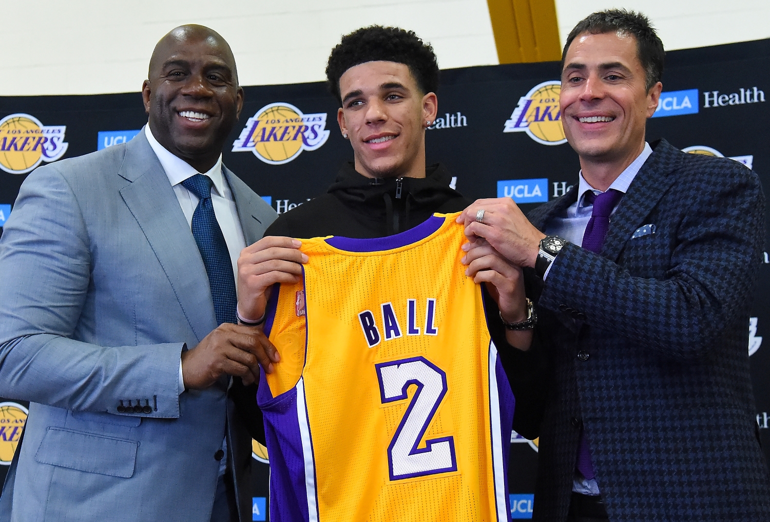 Magic Johnson and Rob Pelinka stand on either side of Lonzo Ball as he holds up his LA Lakers jersey.