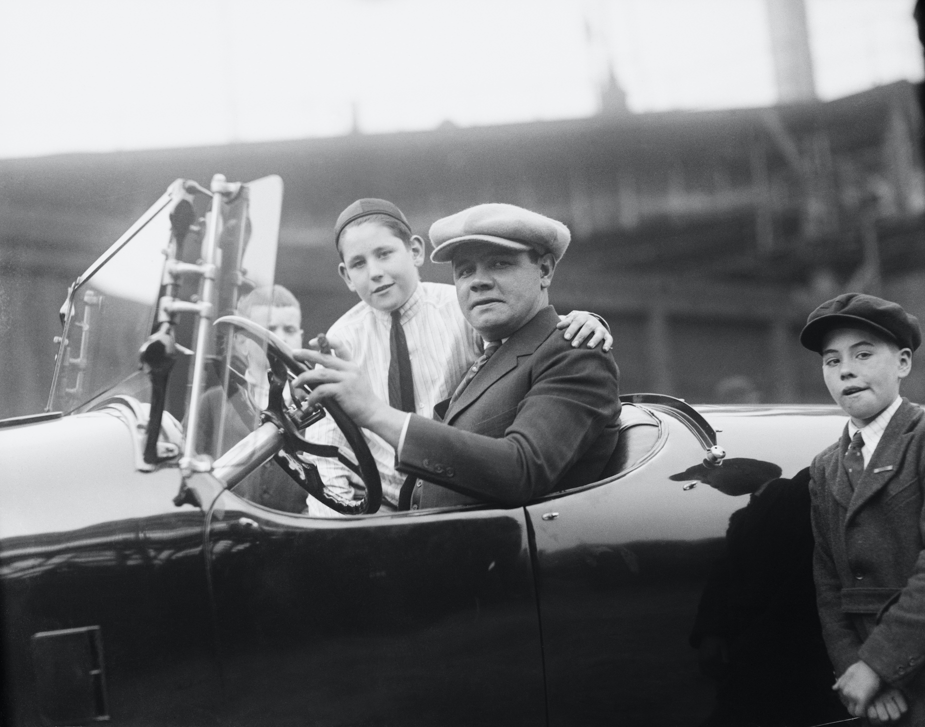 New York Yankees star Babe Ruth poses with two fans while driving his car.