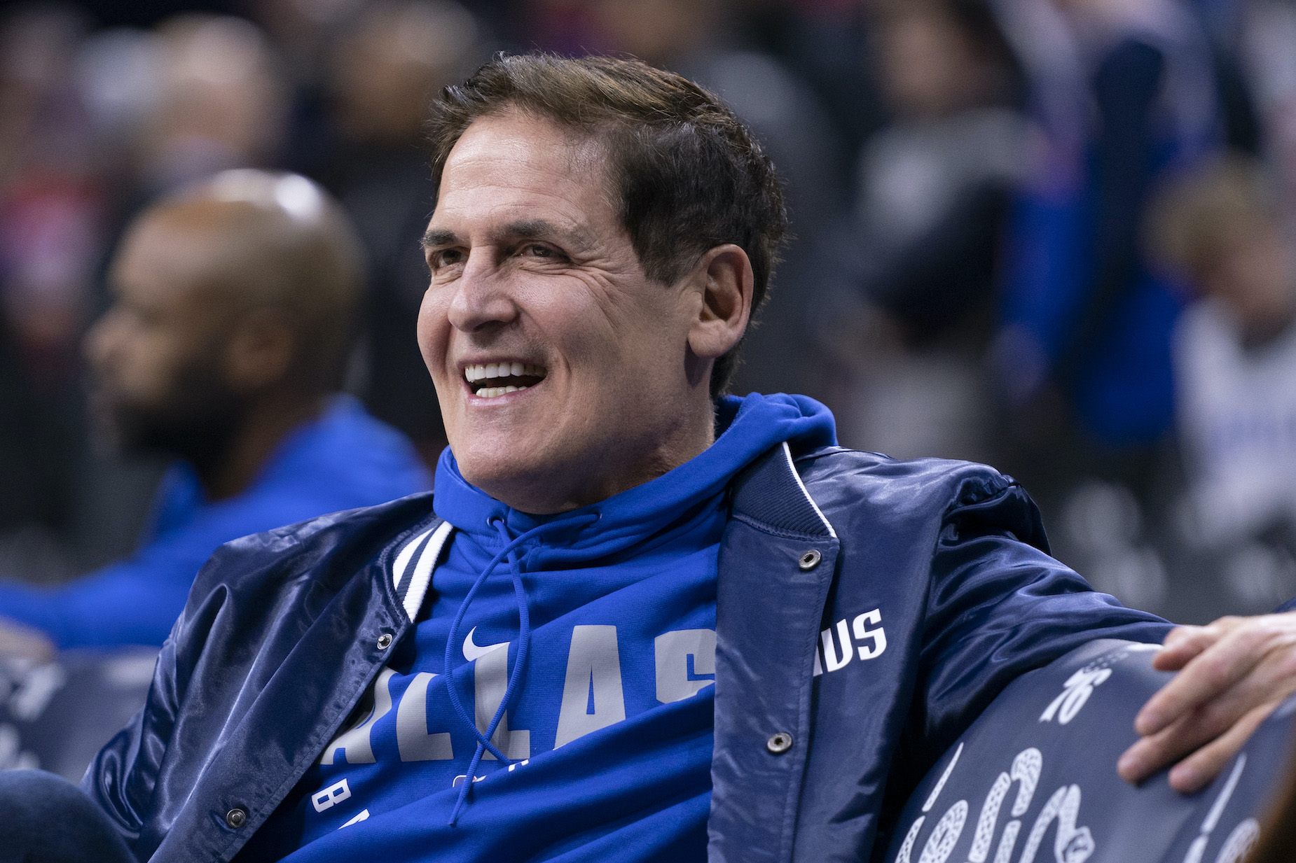 Dallas Mavericks owner Mark Cuban smiles on the bench ahead of an NBA game.