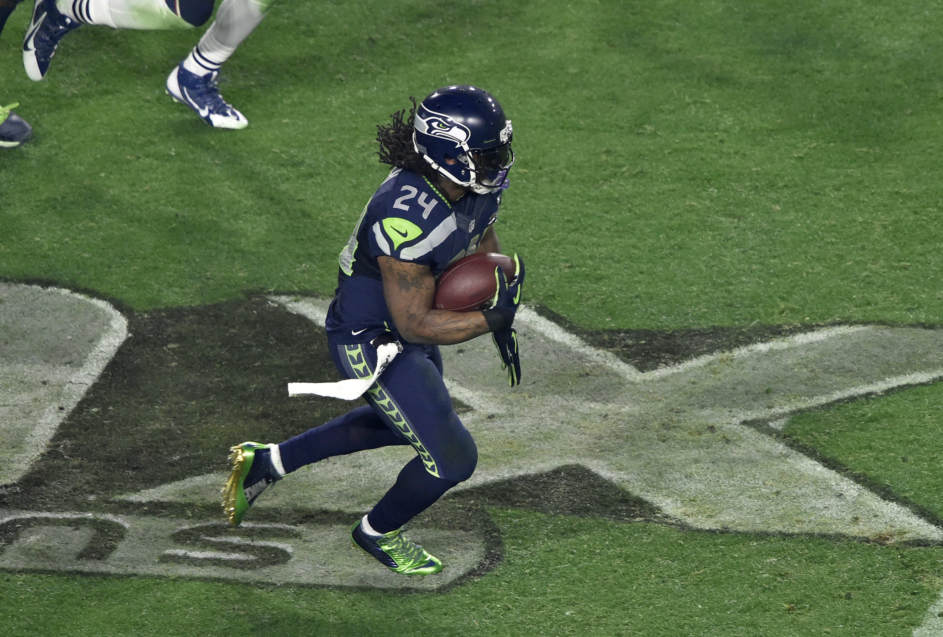 Marshawn Lynch runs the ball on the Super Bowl logo
