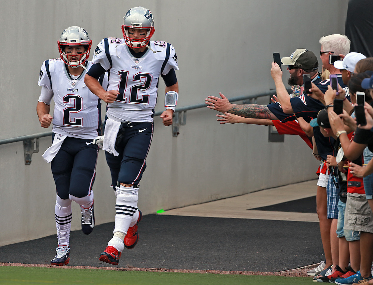 Quarterbacks Brian Hoyer and Tom Brady of the New England Patriots run out onto the field before the NFL game against the Jacksonville Jaguars at TIAA Bank Field on September 16, 2018 in Jacksonville, Florida.