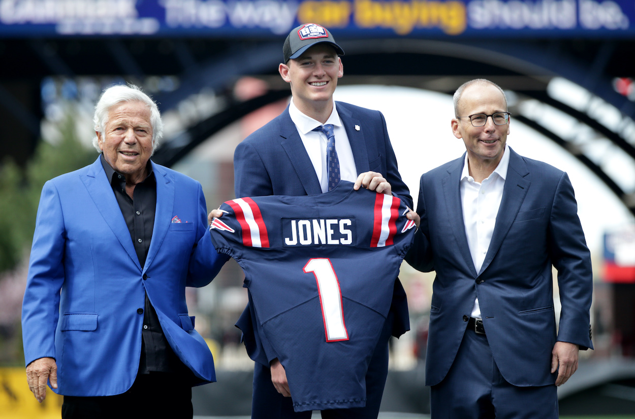 The New England Patriots first-round draft pick Mac Jones, center, holds up his jersey next to Patriots owners Robert Kraft, left, and Jonathan Kraft, right, in Foxborough, MA on April 30, 2021.
