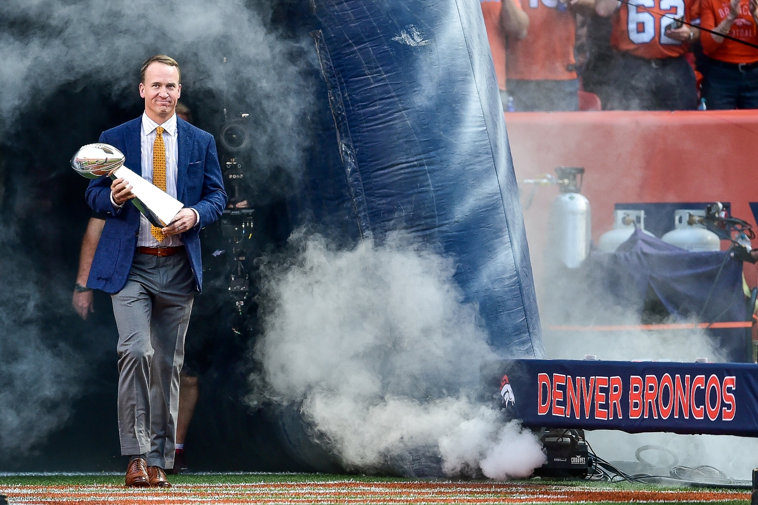 Peyton Manning walks onto the field holding the Lombardi Trophy.