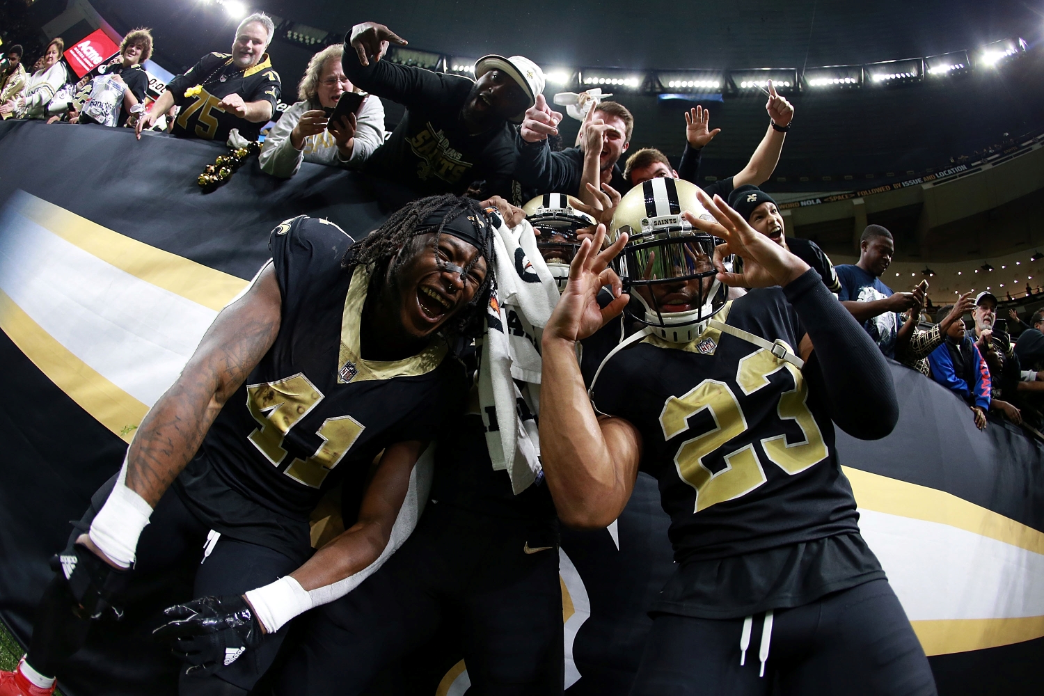 Alvin Kamara, Michael Thomas, and Marshon Lattimore celebrate a victory with New Orleans Saints fans after a game from the 2017 season.