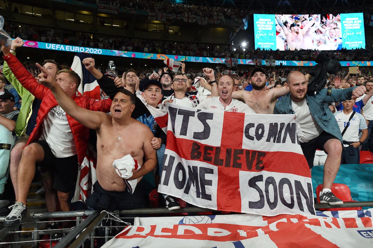England supporters celebrate with an "It's coming home" banner, based on the hit song “Three Lions (Football’s Coming Home)” by David Baddiel, Frank Skinner, and the Lightning Seeds, after winning the UEFA EURO 2020 semi-final football match between England and Denmark at Wembley Stadium in London on July 7, 2021.