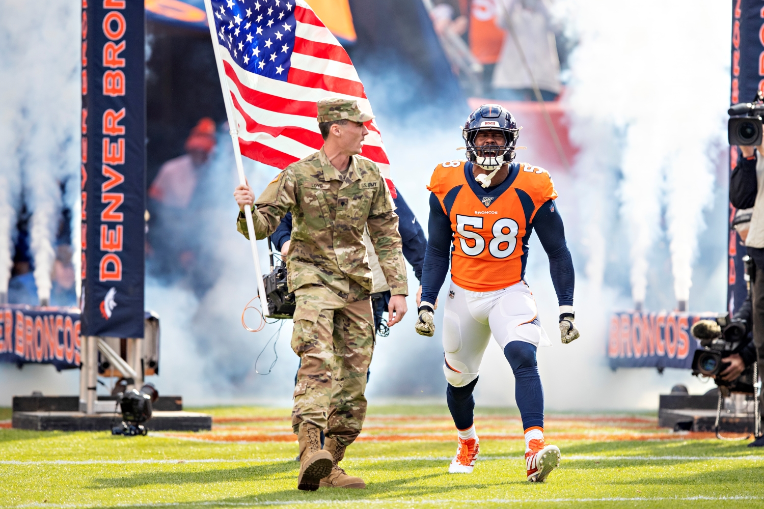 Denver Broncos linebacker Von Miller runs onto the field before a game while accompanied by a U.S. soldier.