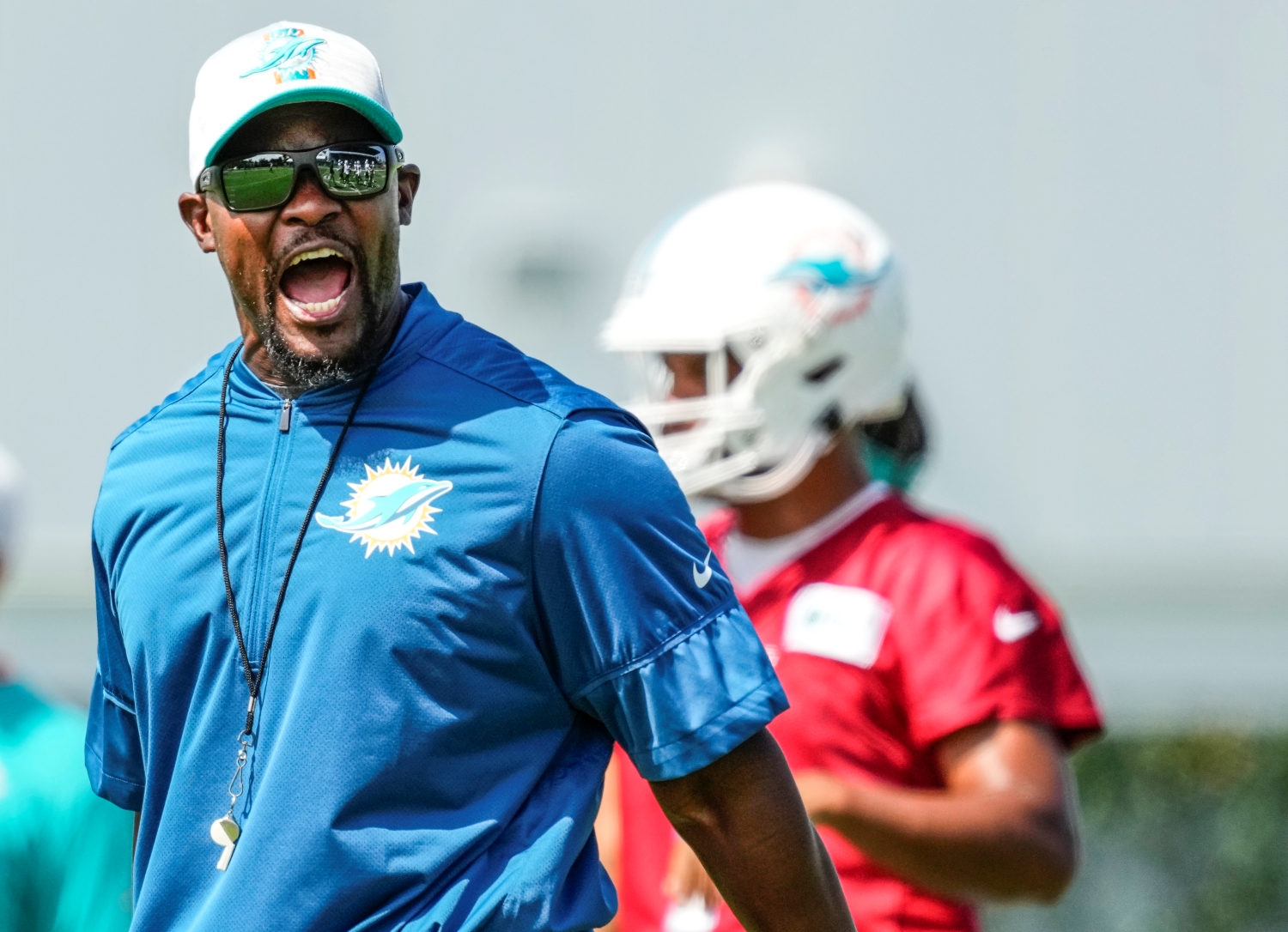 Miami Dolphins head coach Brian Flores giving instructions for practice drills during training camp as Tua Tagovailoa stands in the background.