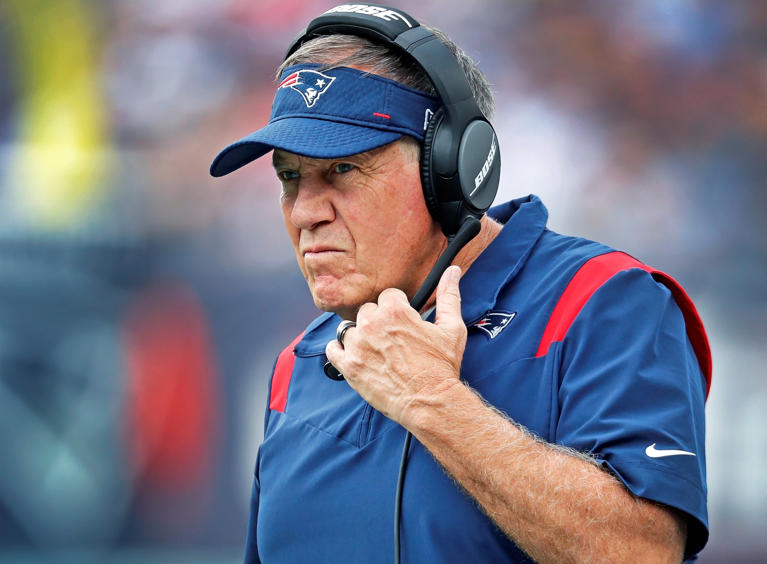 New England Patriots head coach Bill Belichick watches his team play while holding his headset.