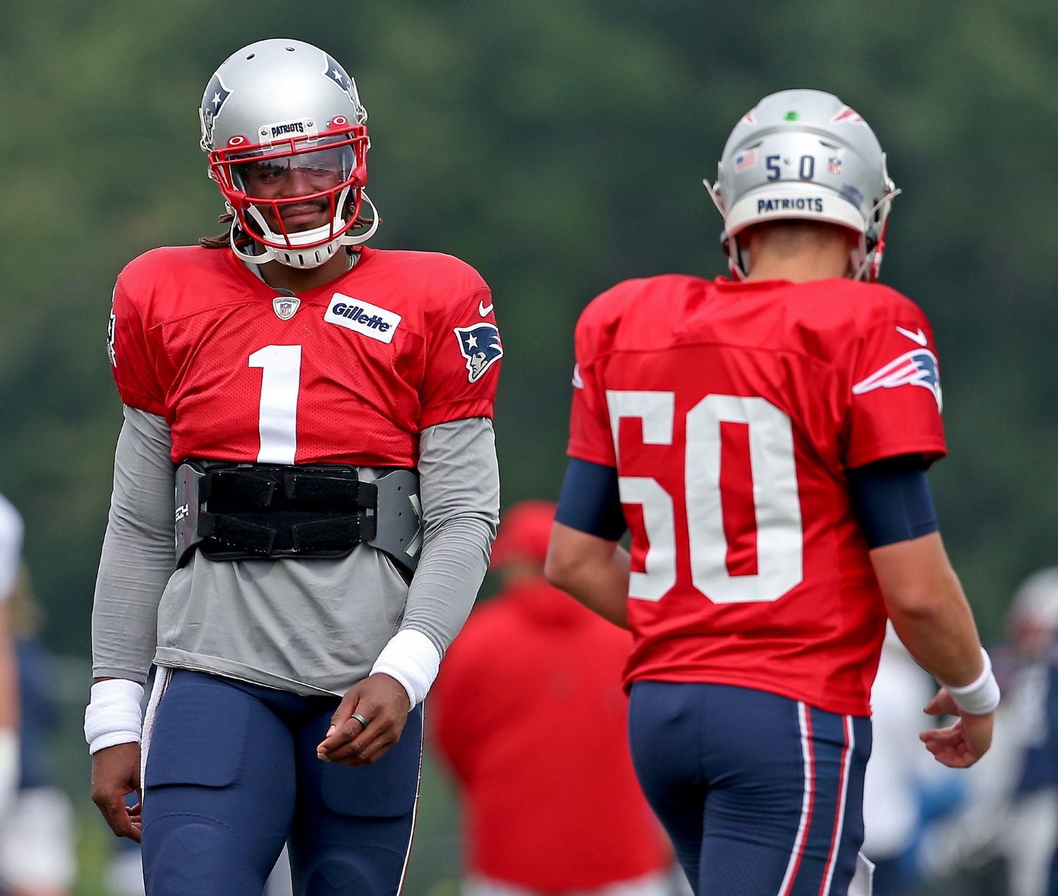 Cam Newton walks by New England Patriots teammate Mac Jones during training camp practice.