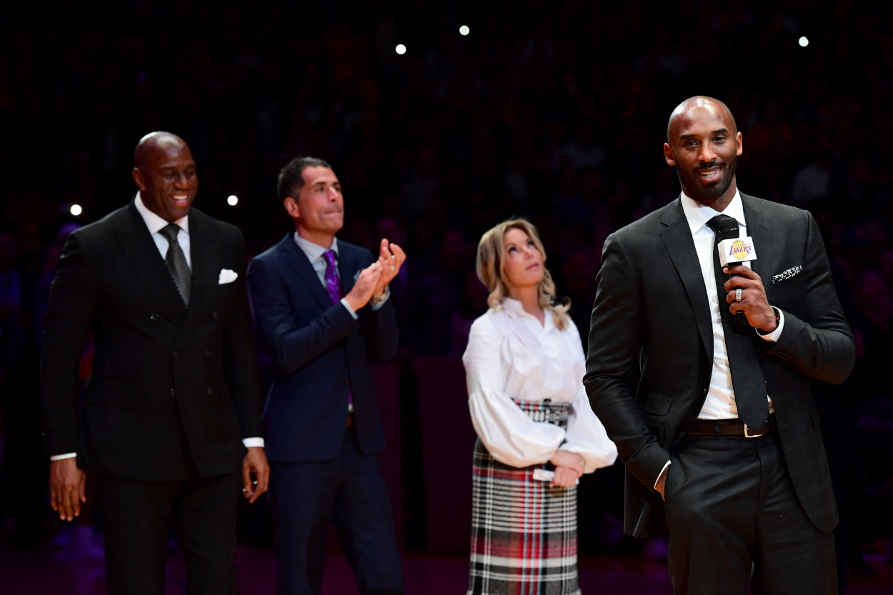 Los Angeles Lakers legend Kobe Bryant addressing a crowd with team owner Jeanie Buss behind him.