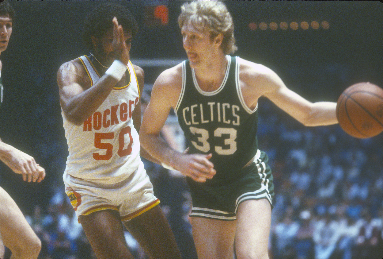 Larry Bird of the Boston Celtics dribbles the ball while being defended by Robert Reid of the Houston Rockets.