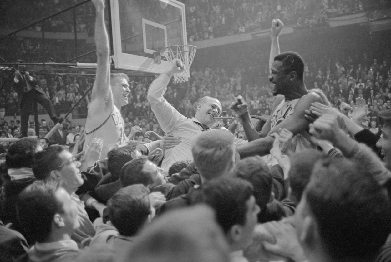 Bill Russell, along with Tommy Heinsohn and coach Red Auerbach, are raised by Boston Celtics fans on the court following their NBA championship victory.