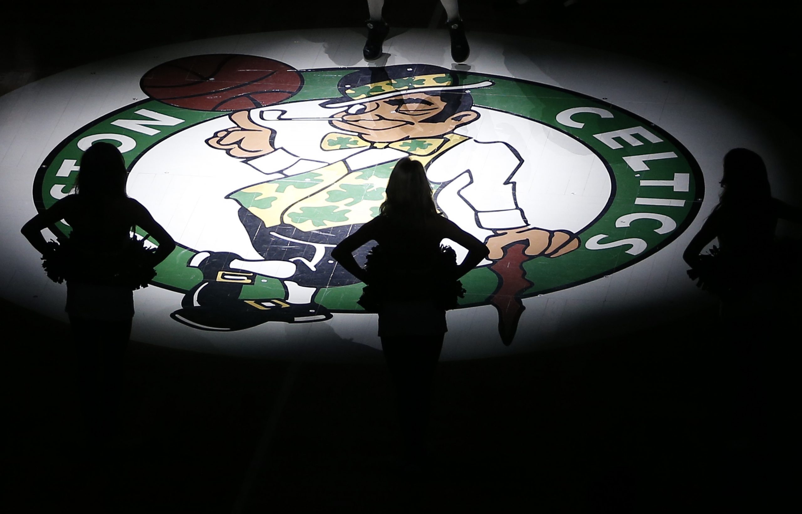 Boston Celtics dancers are silhouetted against the Celtics logo.