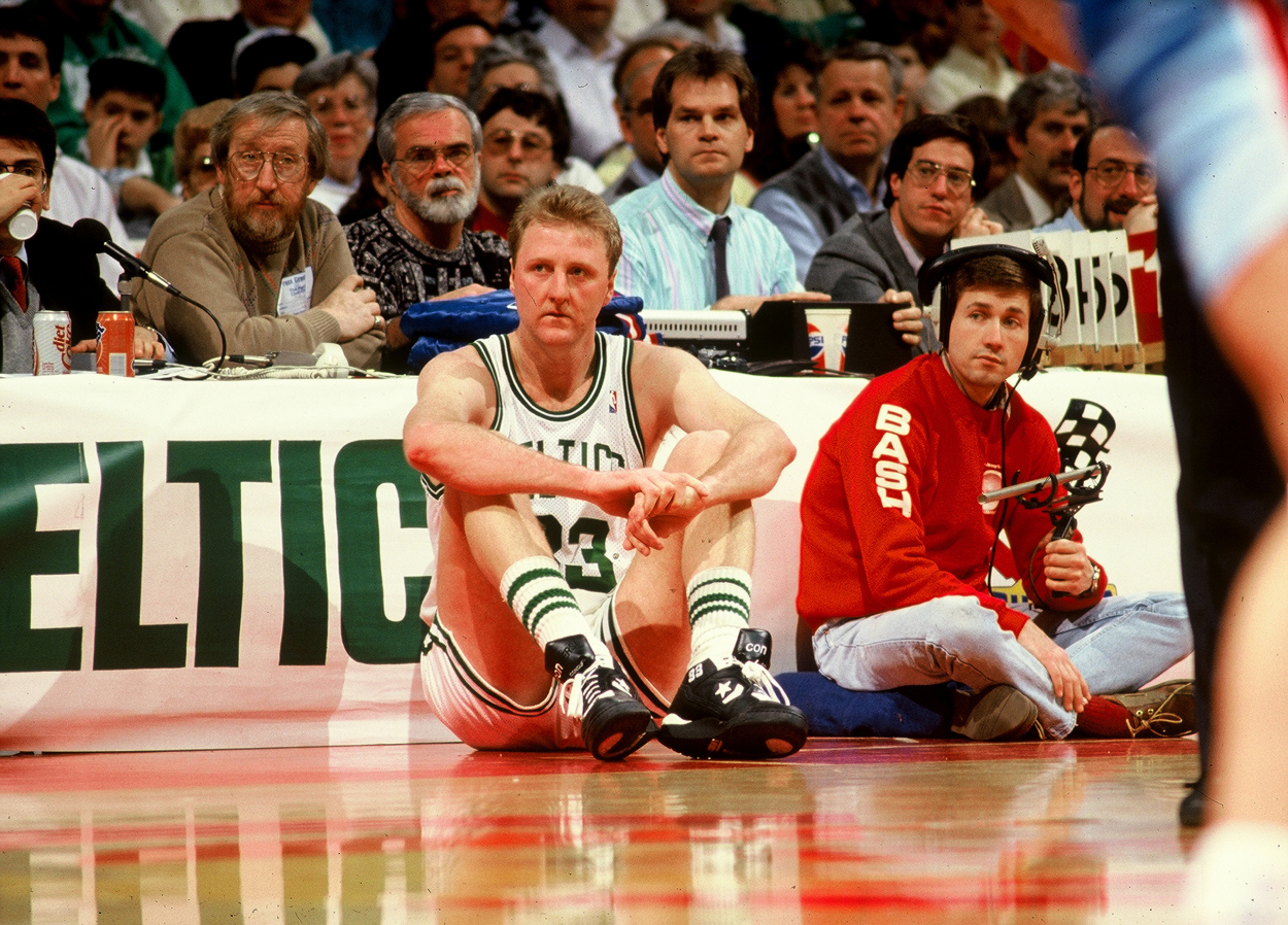 Larry Bird sits on the sidelines in front of the scorer's table.