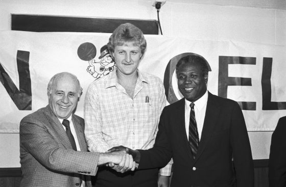 Boston Celtics star Larry Bird (center), Celtics' President Arnold "Red" Auerbach (left) and Celtics' Head Coach K.C. Jones (right) clasp hands at a press conference.