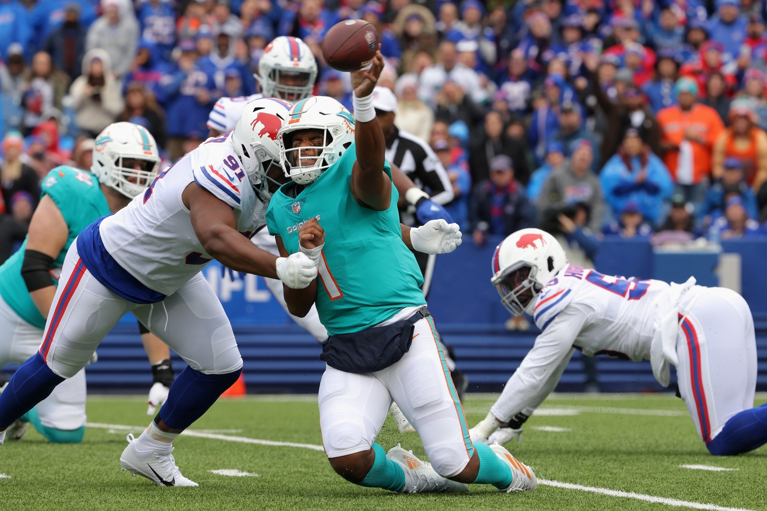 Miami Dolphins quarterback Tua Tagovailoa throws a pass while getting hit by a Buffalo Bills defender.