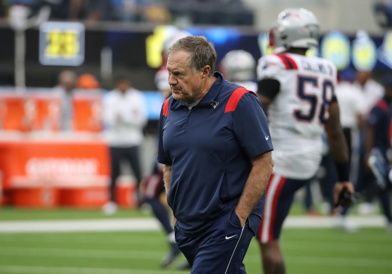 New England Patriots coach Bill Belichick walks across the field while players warm up before a game.