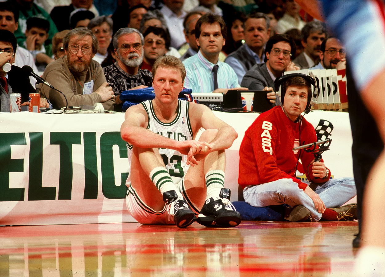 Boston Celtics great Larry Bird sitting in front of the scorer's table.