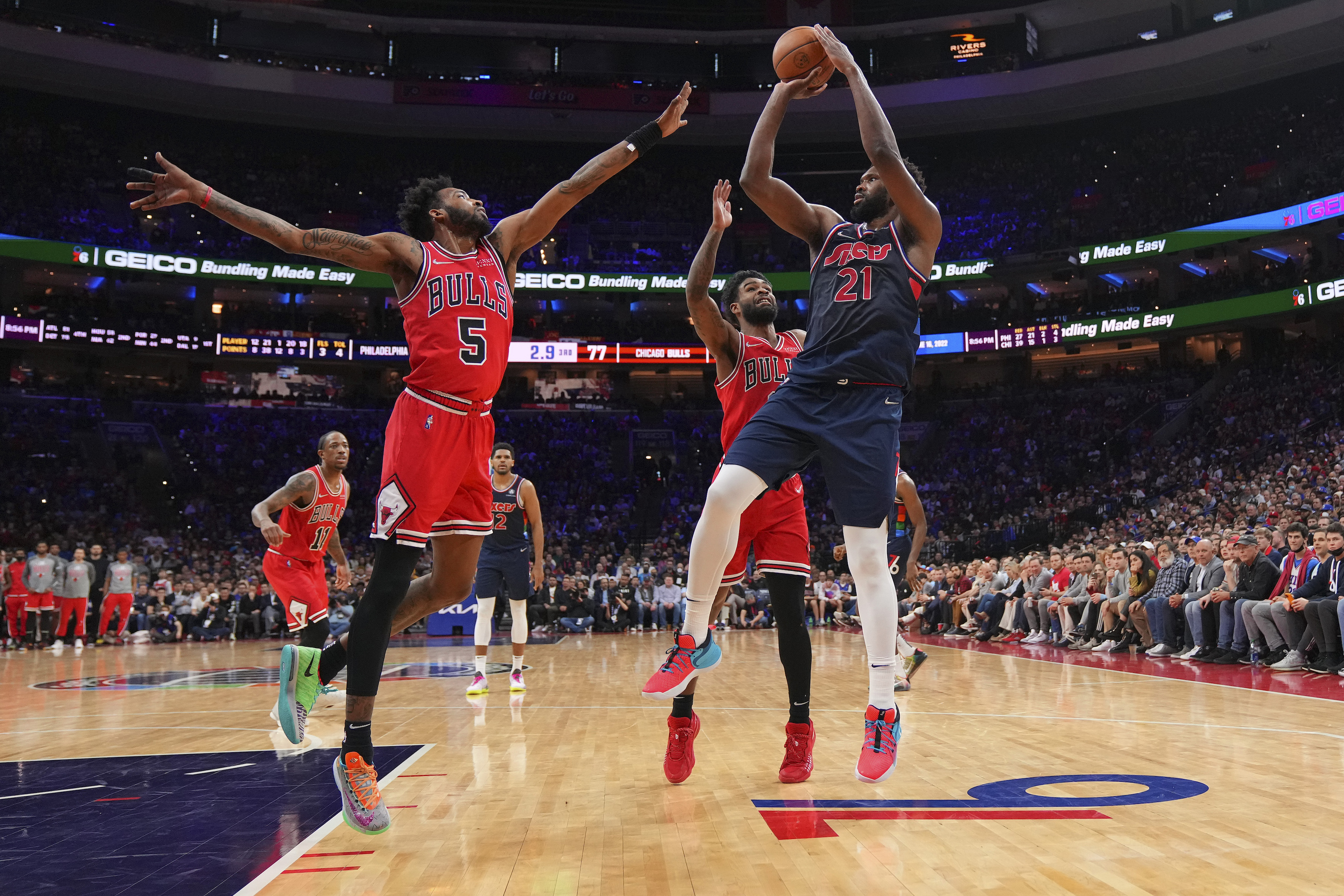 Chicago Bulls forward Derrick Jones Jr. #5 and guard Coby White #0 defend Philadelphia 76ers center Joel Embiid #21 during an NBA game in March 2022