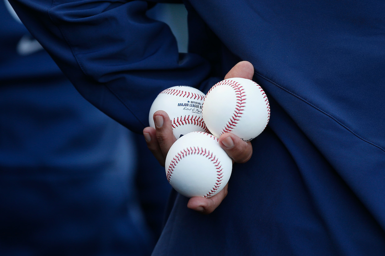 A coach holds three MLB baseballs in his hands in late 2021 -- before a lockout imposed by owners against players.